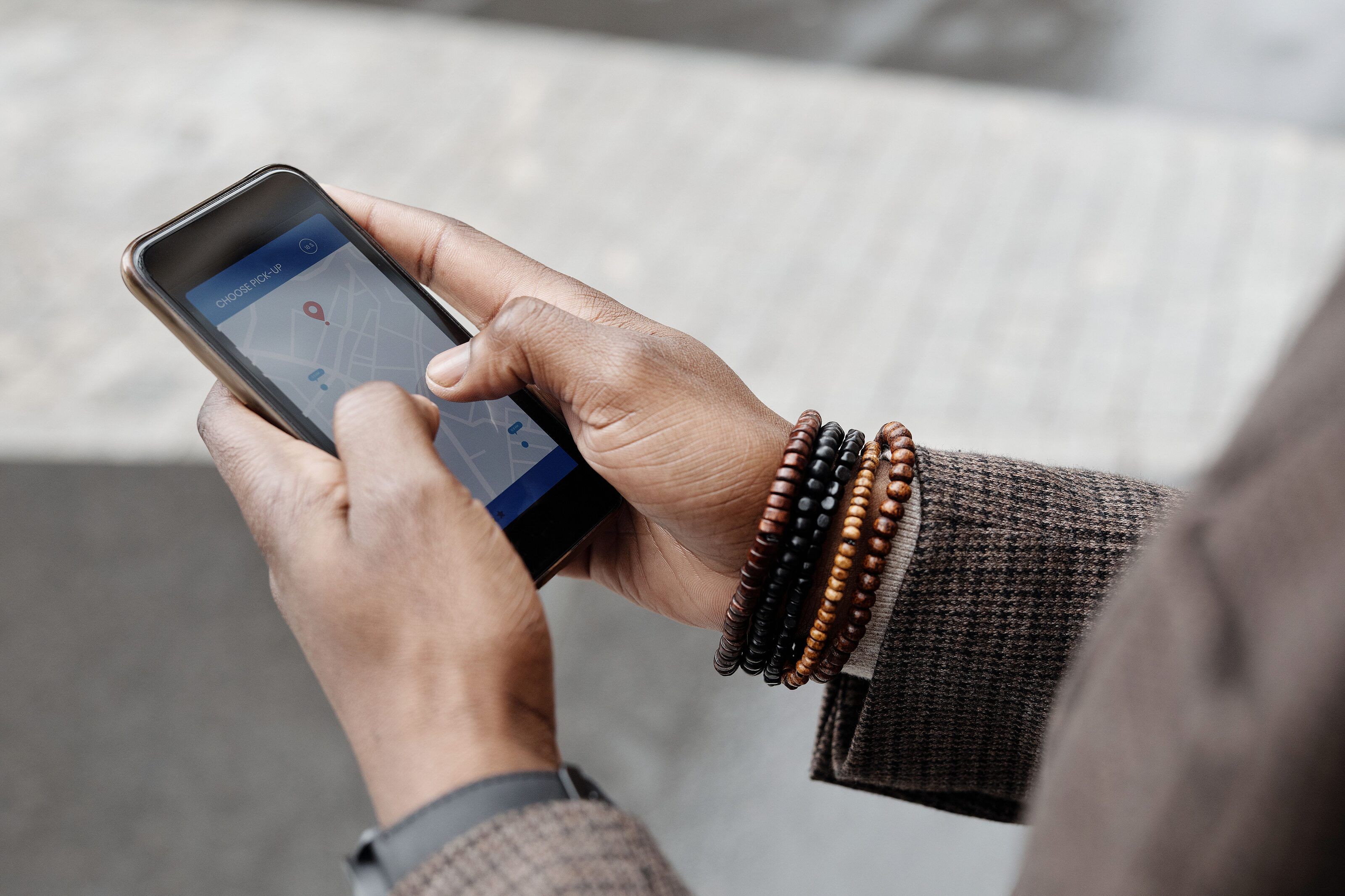 Hands holding a smartphone that shows a street map with a location pin, above a paved sidewalk.