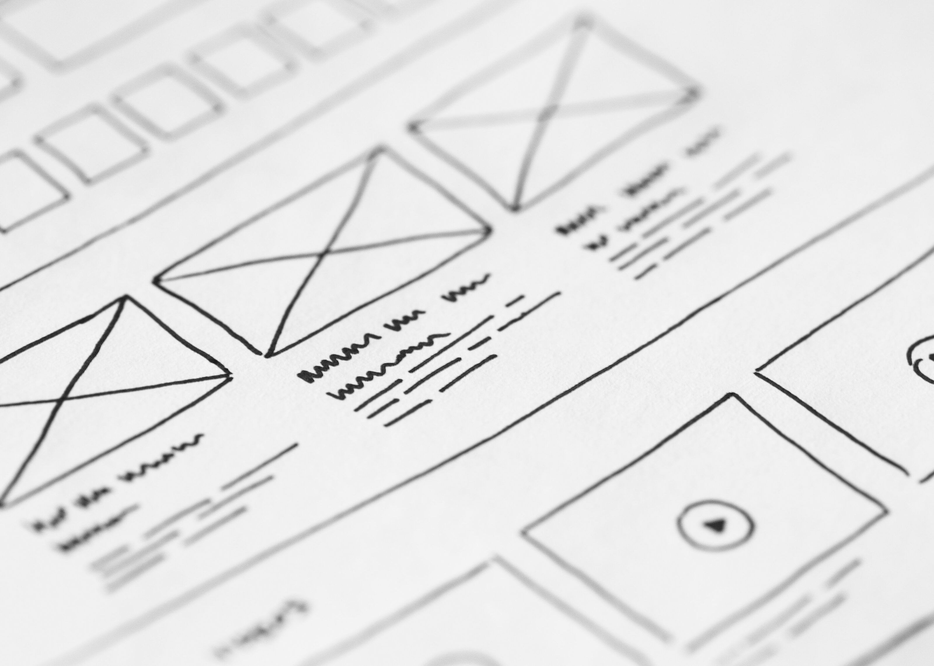 Hand-drawn website wireframe on white paper, with crossed-out image boxes, lines standing in for text and a video block.